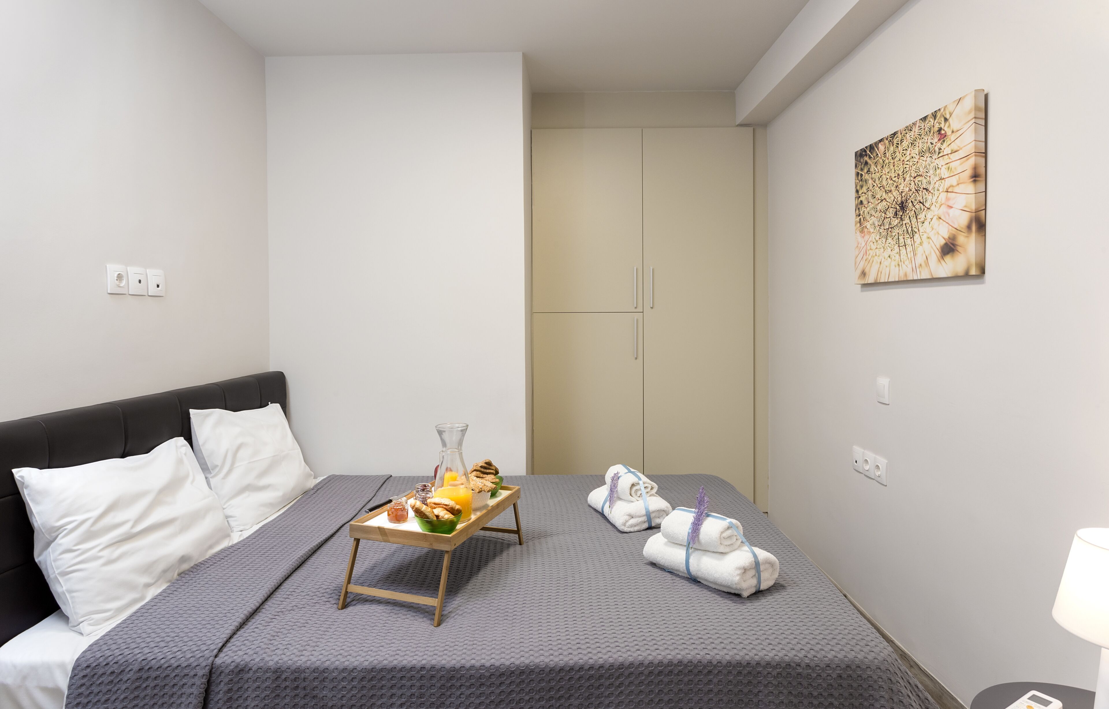 Una camera d'albergo con un letto, un vassoio per la colazione, asciugamani e un quadro appeso al muro.