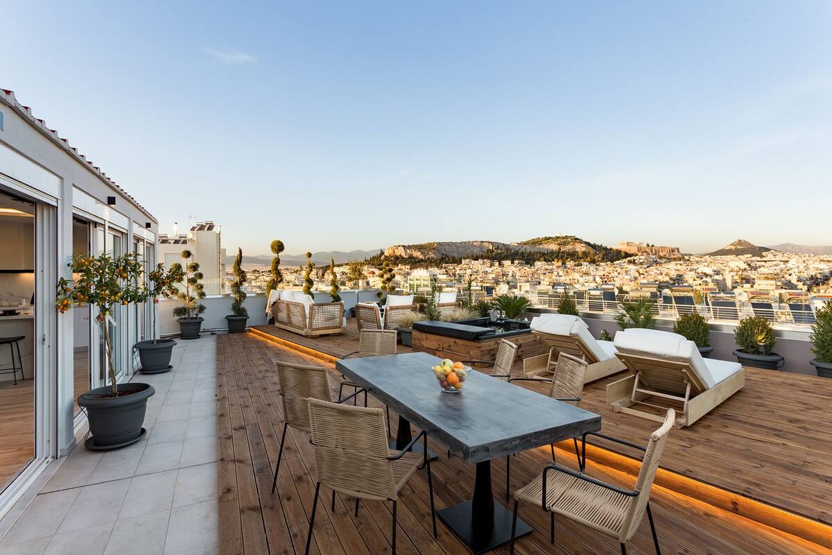 Terraza en la azotea con mobiliario exterior, plantas en macetas y vistas de la ciudad.