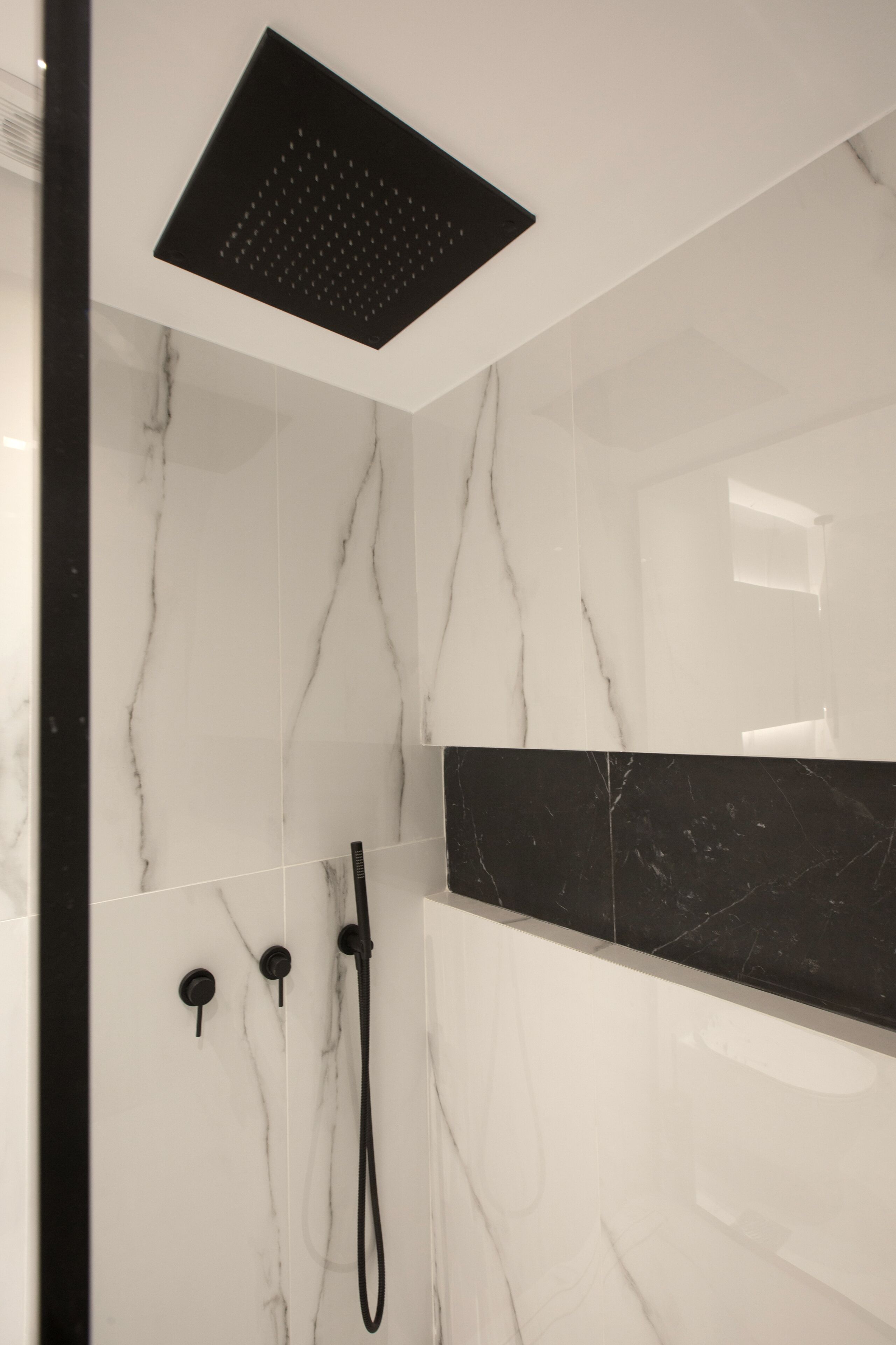 A modern bathroom with a shower, marble walls, and a black marble accent wall.