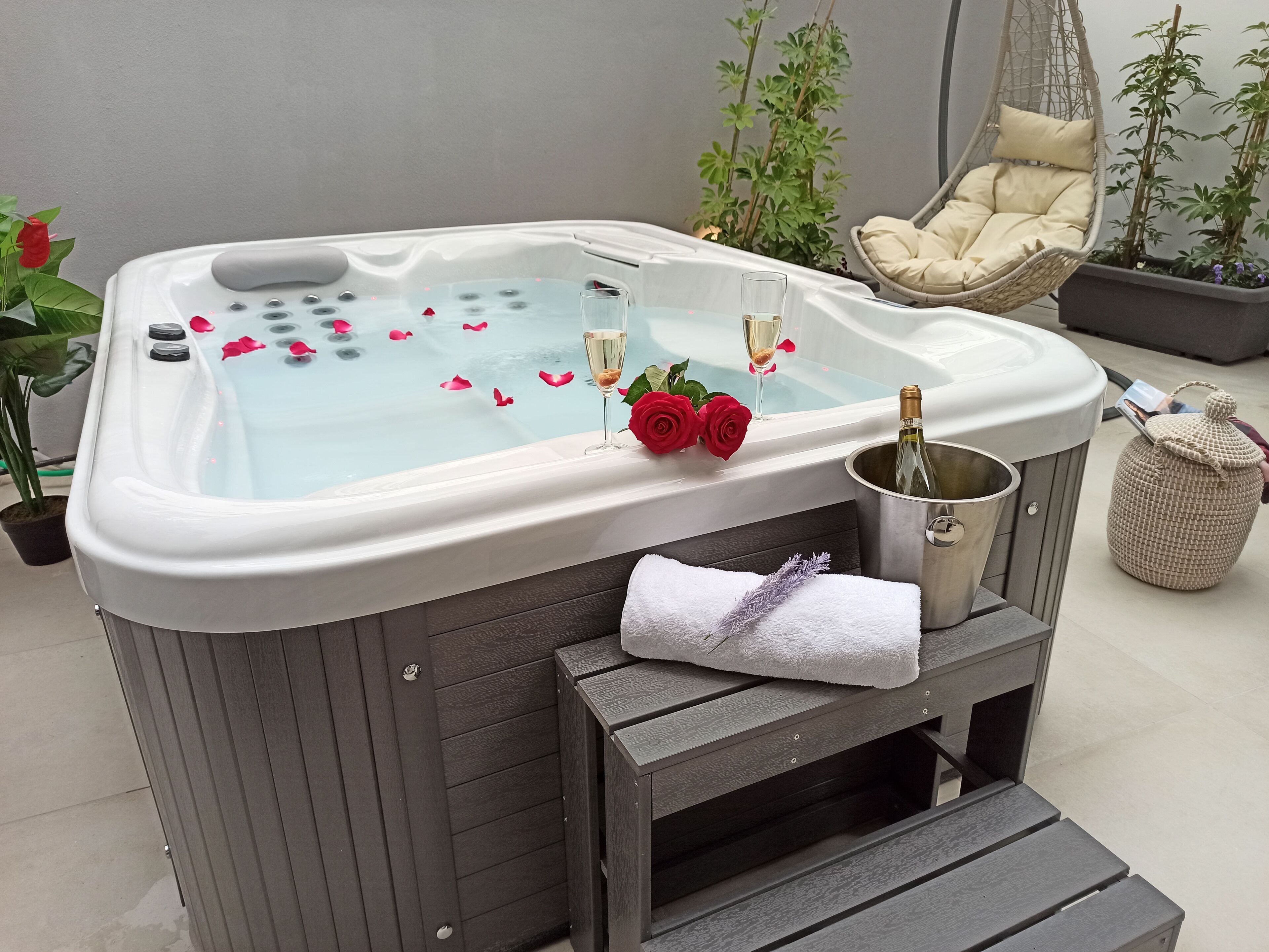 Una vasca idromassaggio con petali di rosa, champagne e un asciugamano.