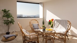 Un balcón con mobiliario de mimbre, una planta en maceta y una mesa con una bebida y flores.