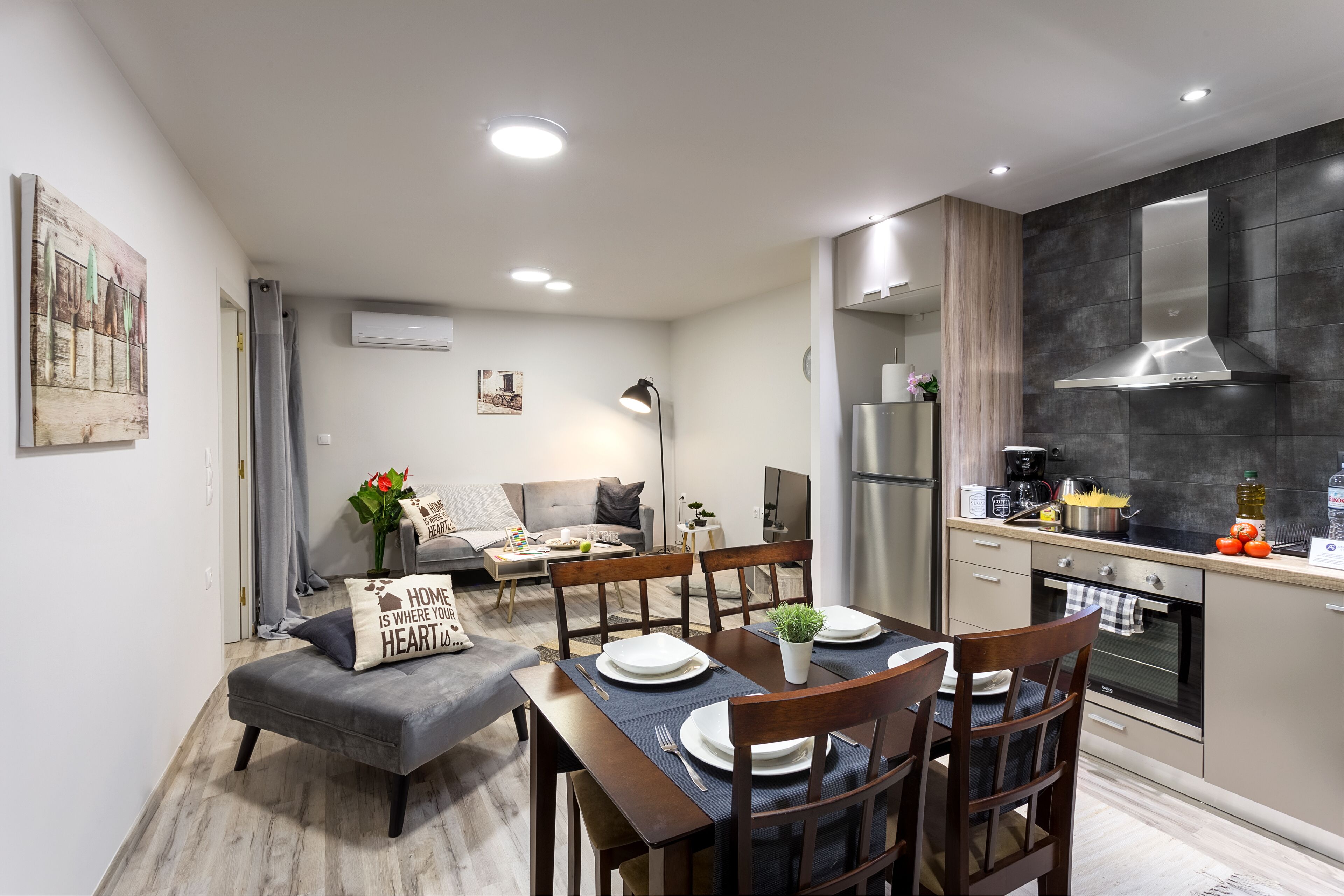 A modern kitchen with a built-in oven, a dining area with a table set for four, and a living room with a sofa and a coffee table.