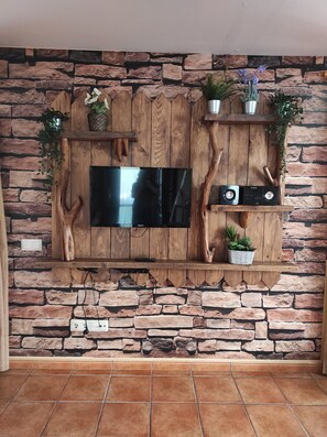 Un mur en pierre sur lequel est fixé un téléviseur à écran plat, entouré d’étagères en bois où sont disposées des plantes et un système stéréo.