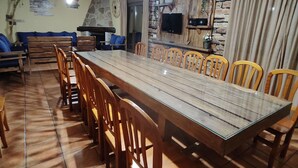 Ein Essbereich mit einem langen Holztisch und Stühlen, einer Steinwand mit Fernseher und einem Deckenventilator.