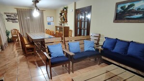 Ein großzügiges Wohnzimmer mit einem großen Holzesstisch, blauen Sofas und einem Deckenventilator.