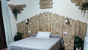 Ein Schlafzimmer mit einem Holz-Kopfteil, einem Bett mit grauer Bettwäsche und Topfpflanzen.