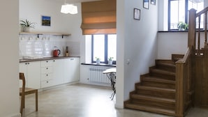 A kitchen with white cabinets, a wooden chair, a hanging light fixture, a radiator, and a window with a view. - Fazenda U Mihalyicha (Talgar)