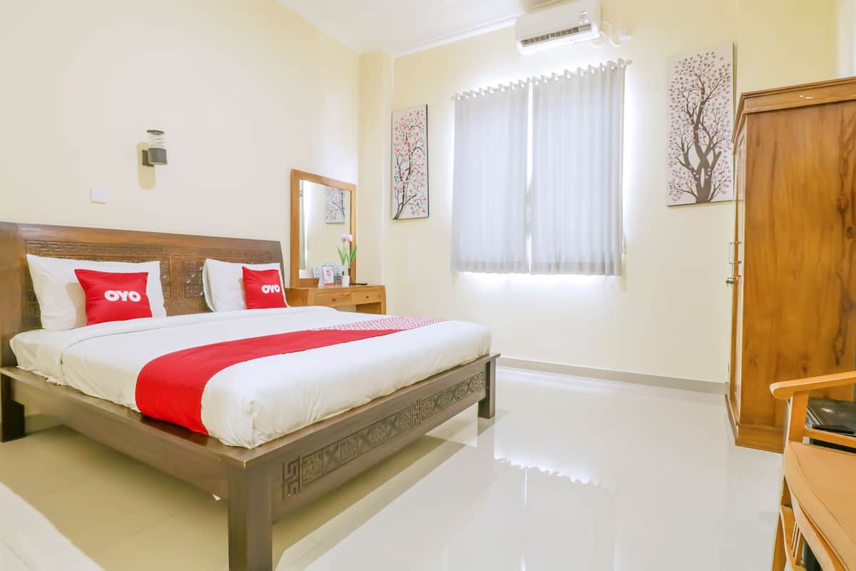 A hotel room with a large bed, a wooden headboard, a bedside table with a lamp, a wardrobe, and a window with curtains.