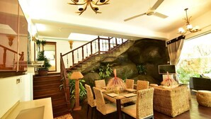 A spacious living area with a wooden staircase, wicker furniture, and a large rock wall. - Thevni Holiday Resort (Ingiriya)