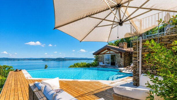 Une terrasse en bois avec une piscine, des chaises longues et un parasol.