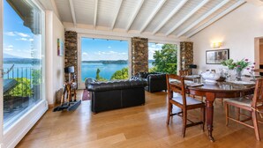Un vaste espace de vie avec une grande fenêtre donnant sur un lac, une cheminée et une table à manger dressée pour six personnes.