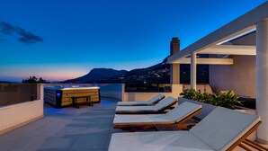 Una terraza en la azotea con sillones, un jacuzzi y vistas a un paisaje urbano al atardecer.