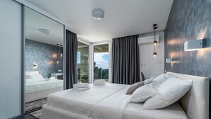 Un dormitorio moderno con una cama grande, una puerta de cristal que da a un balcón y vistas al exterior.