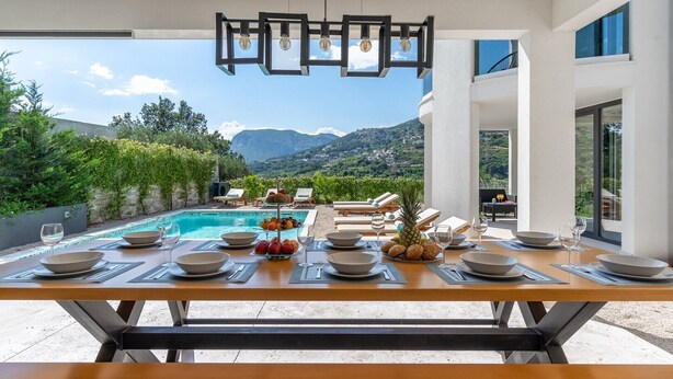 Un comedor con vista a la piscina, mobiliario exterior y montañas al fondo.