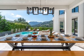 Un espace repas avec vue sur la piscine, des sièges en plein air et une chaîne de montagnes en arrière-plan.