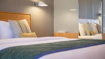 Une chambre d’hôtel avec une tête de lit en bois, un grand lit avec du linge de lit blanc, un plaid vert et une lampe fixée au mur.