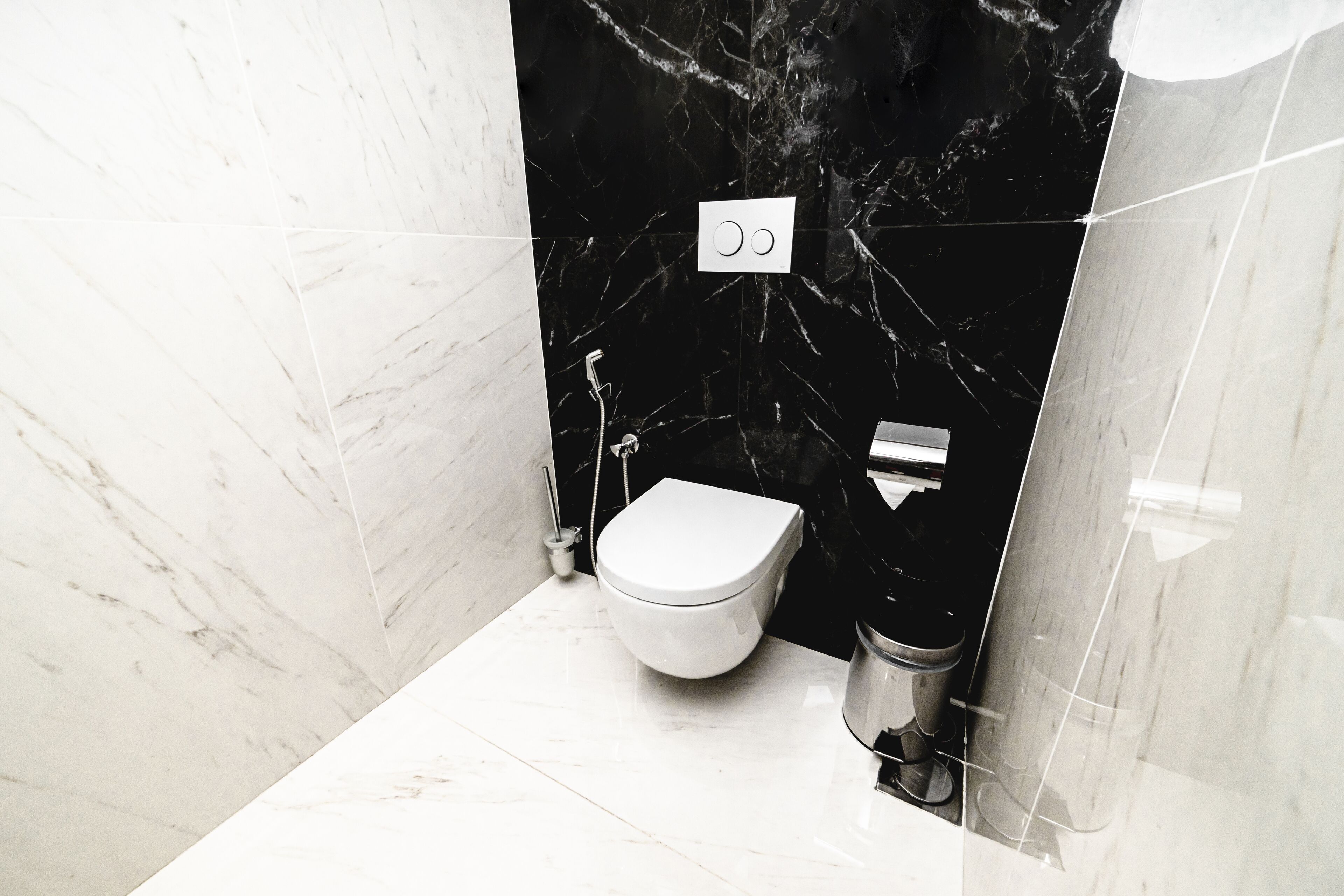 Een moderne badkamer met een wit toilet, zwarte marmeren wanden en een vloer van wit marmer.