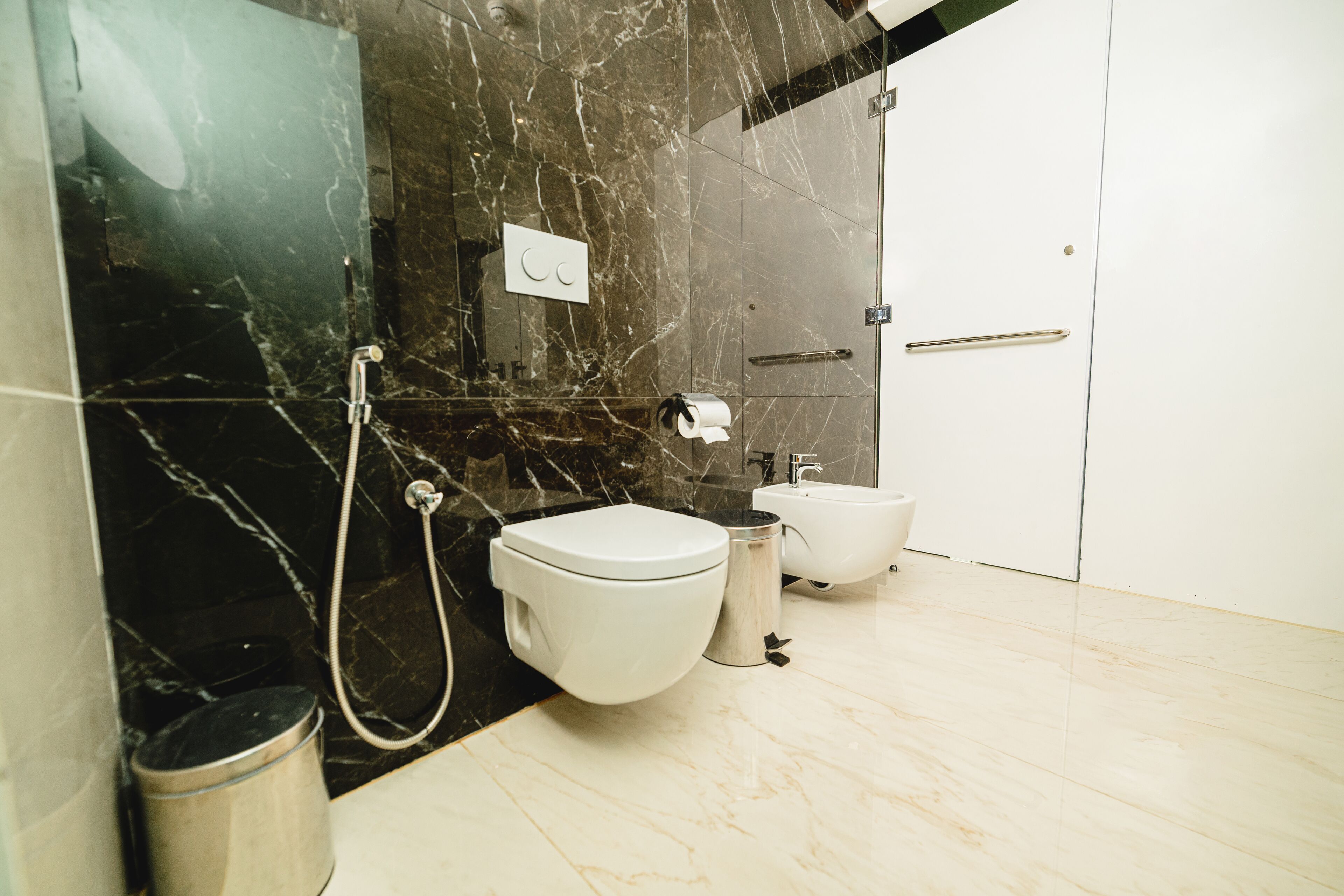 Ein modernes Badezimmer mit Toilette, Bidet und Waschbecken, Marmorwänden und einem Mülleimer.