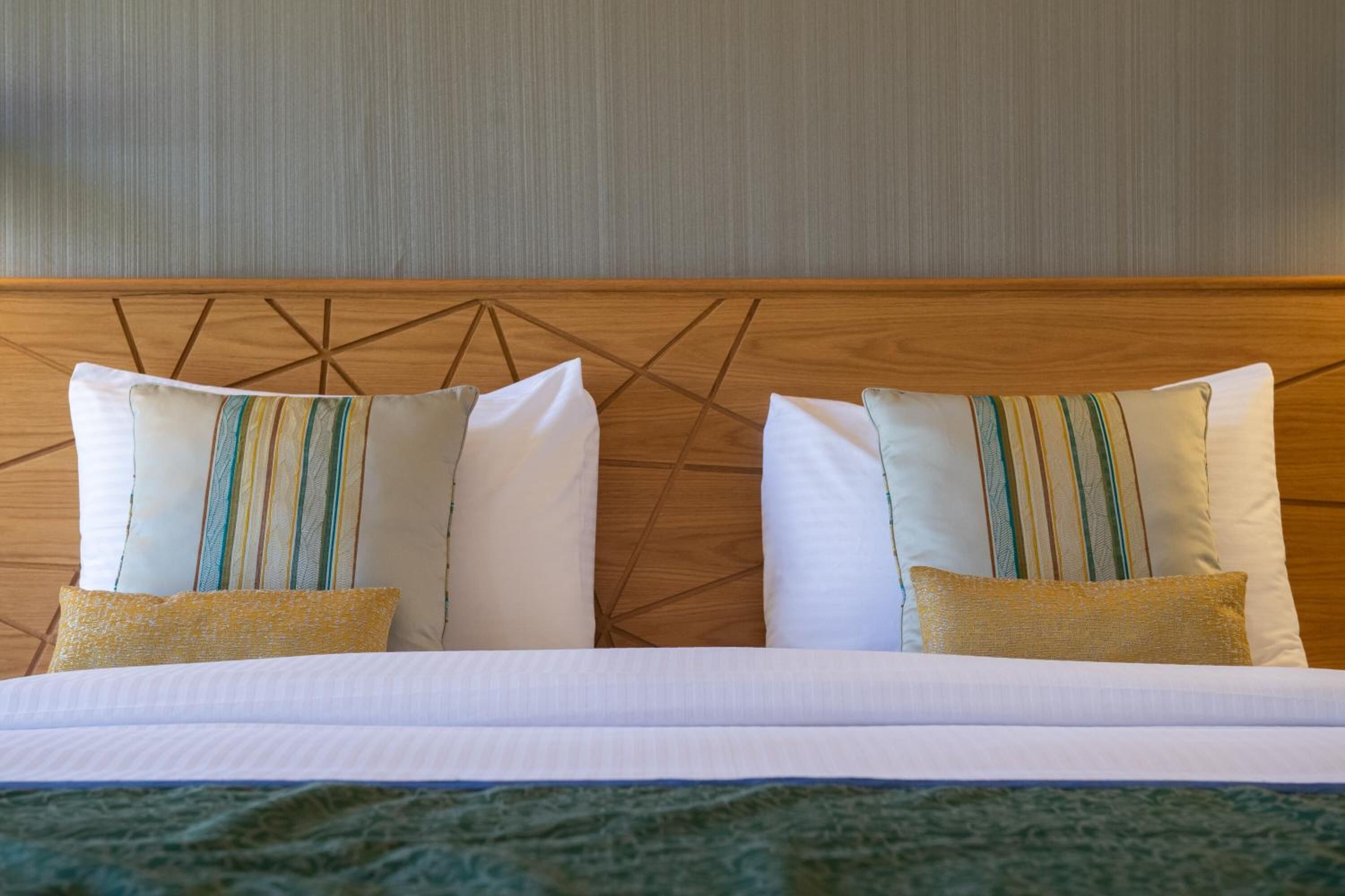 A hotel room with a wooden headboard, two beds with white bedding, and striped pillows.