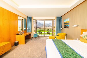 Habitación de hotel con cama, escritorio, sillas y vistas a montañas a través de amplios ventanales.