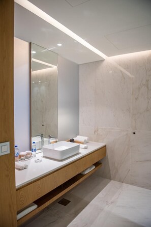 A modern bathroom with a large mirror, a white sink, and marble walls.