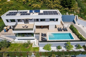 Uma casa moderna de dois andares com um painel solar no telhado, piscina e um jardim ajardinado.