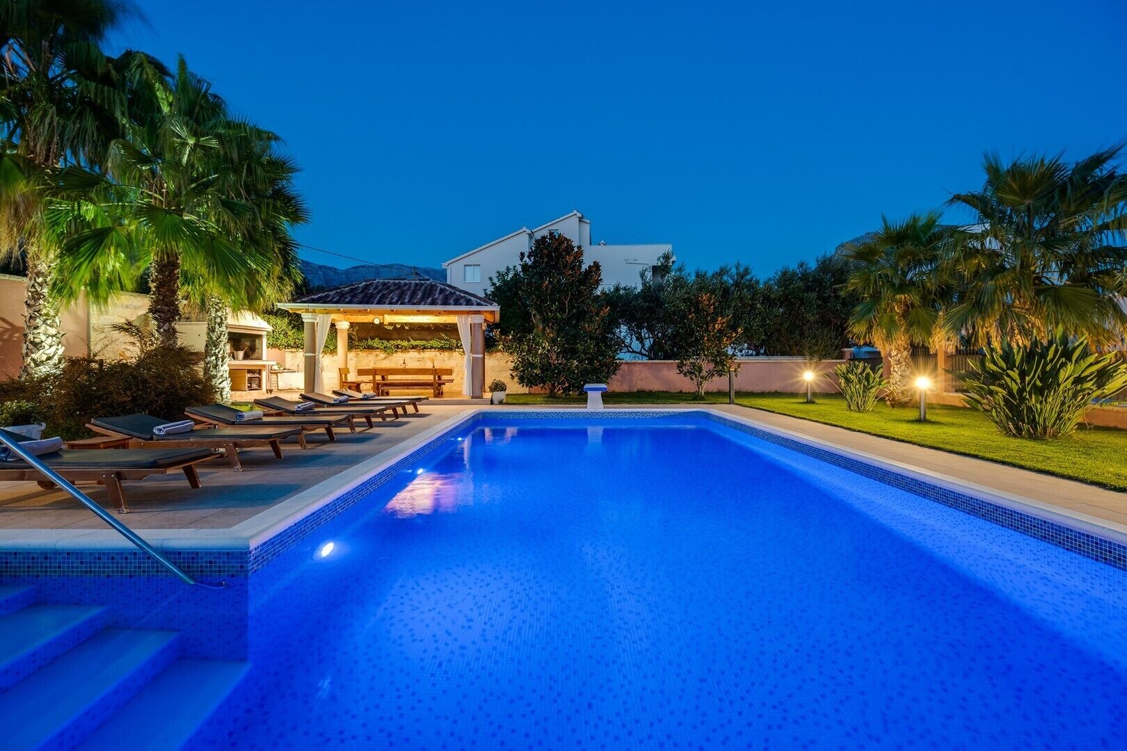 A swimming pool with lounge chairs, a covered seating area, and a well-maintained garden.