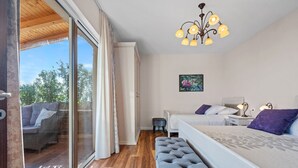 A bedroom with a large sliding glass door leading to an outdoor seating area, a bed with a patterned bedspread, a bench, and a chandelier.