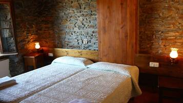Une chambre avec un lit double doté d’une tête de lit en bois et de deux tables de chevet, chacune avec une lampe. Les murs de la chambre sont en pierre et le lambris est en bois.