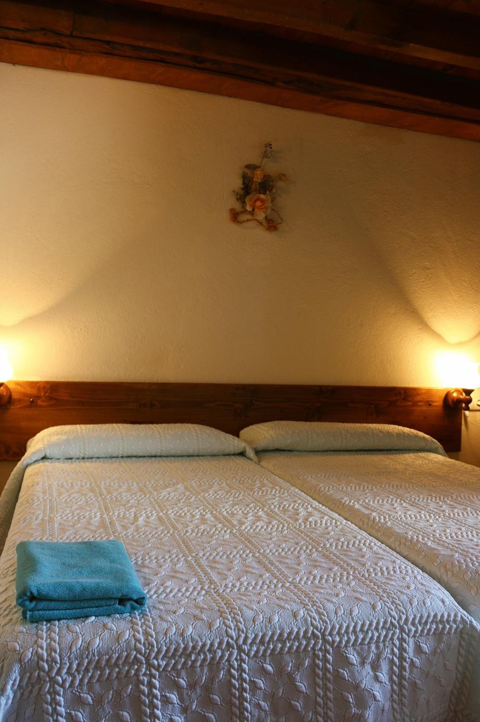Una cama doble con colcha blanca y una toalla azul doblada.