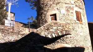 A stone tower with a small window and a door, surrounded by a stone wall and a tree. - Hostal Ruso (Llívia)
