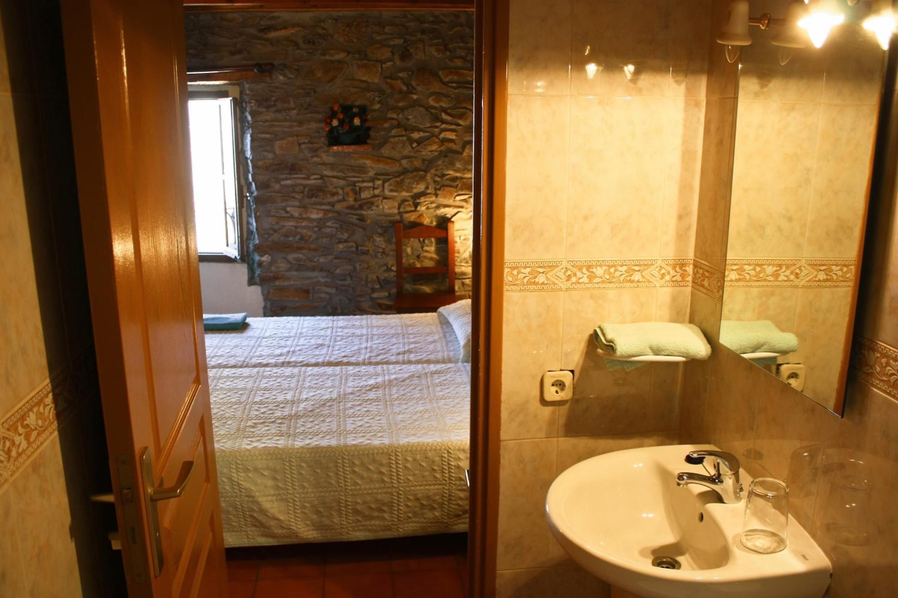 Un dormitori amb una paret de pedra, un llit amb estore i un bany amb un rentaplat i un mirall.