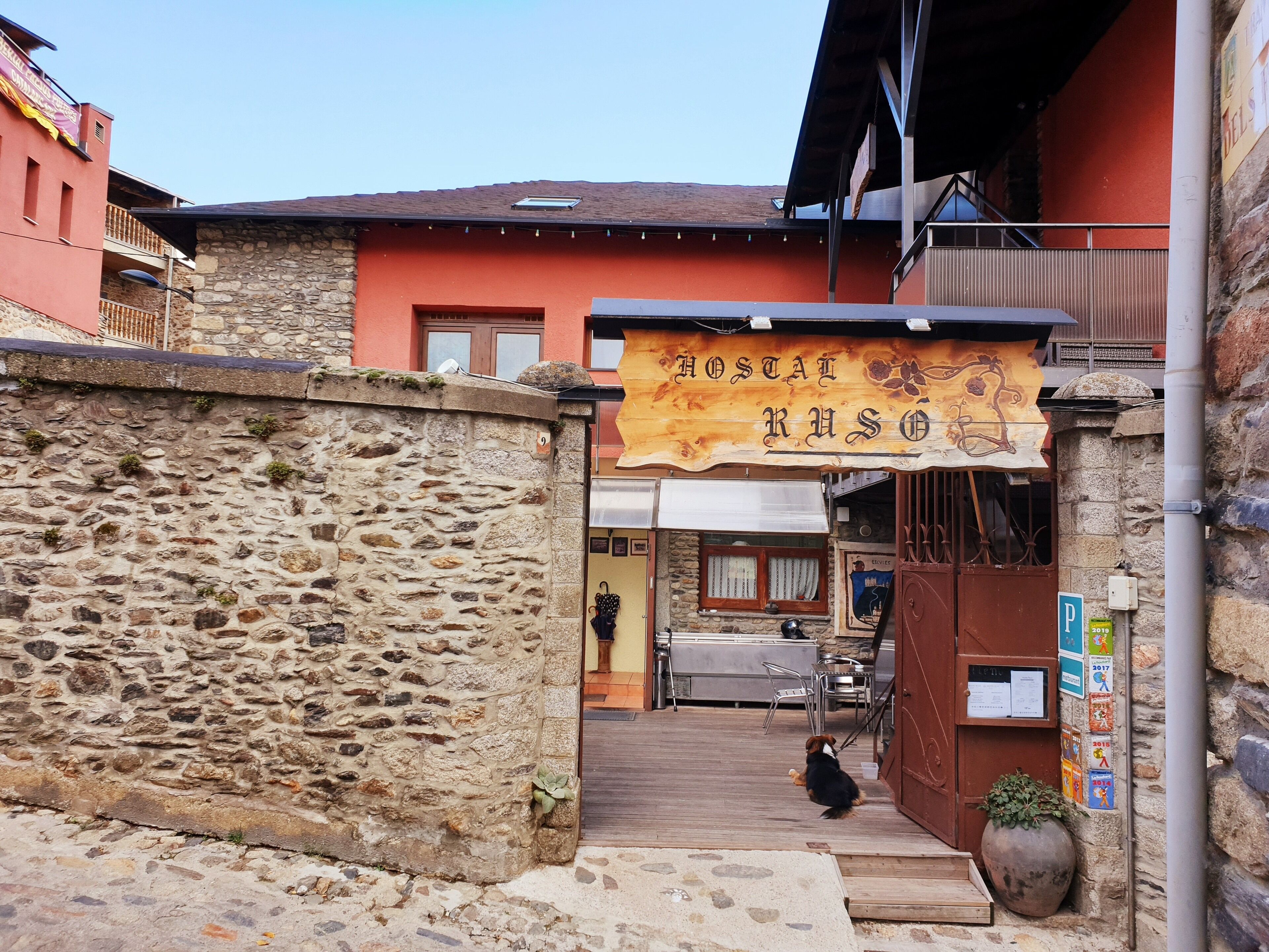 A stone wall, a wooden door, and a sign for "Hostal Rusó".