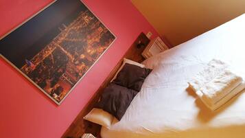 Habitación de hotel con cama, almohadas, mesita de noche, lámpara y un cartel con vistas a la ciudad.
