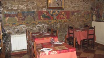 A restaurant with stone walls and a mosaic mural. Tables are set with red tablecloths and wine glasses.