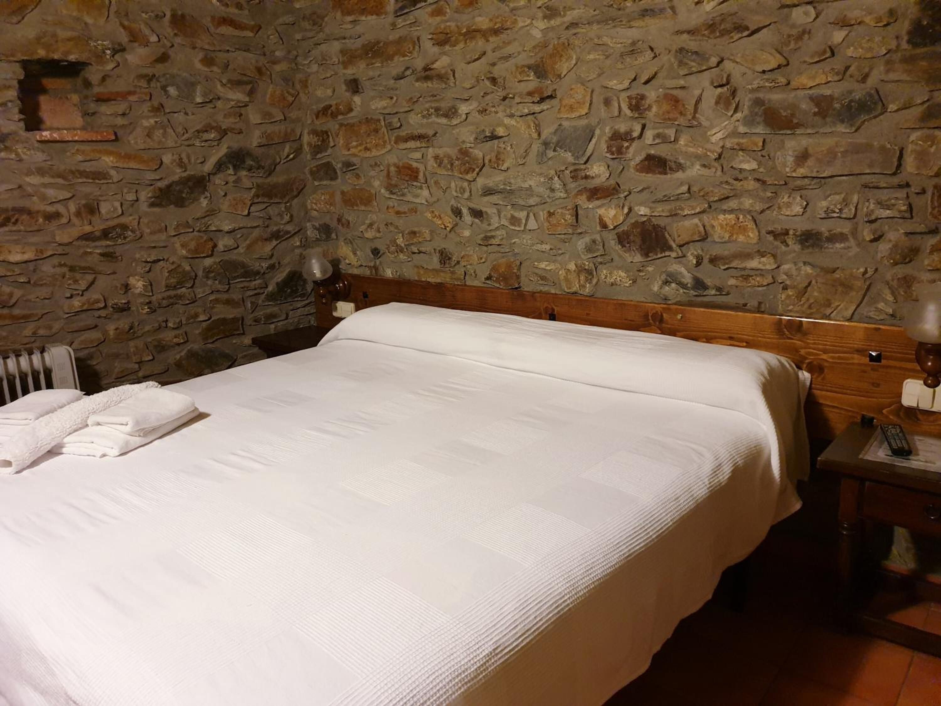Cama com cabeceira de madeira num quarto com parede de pedra.