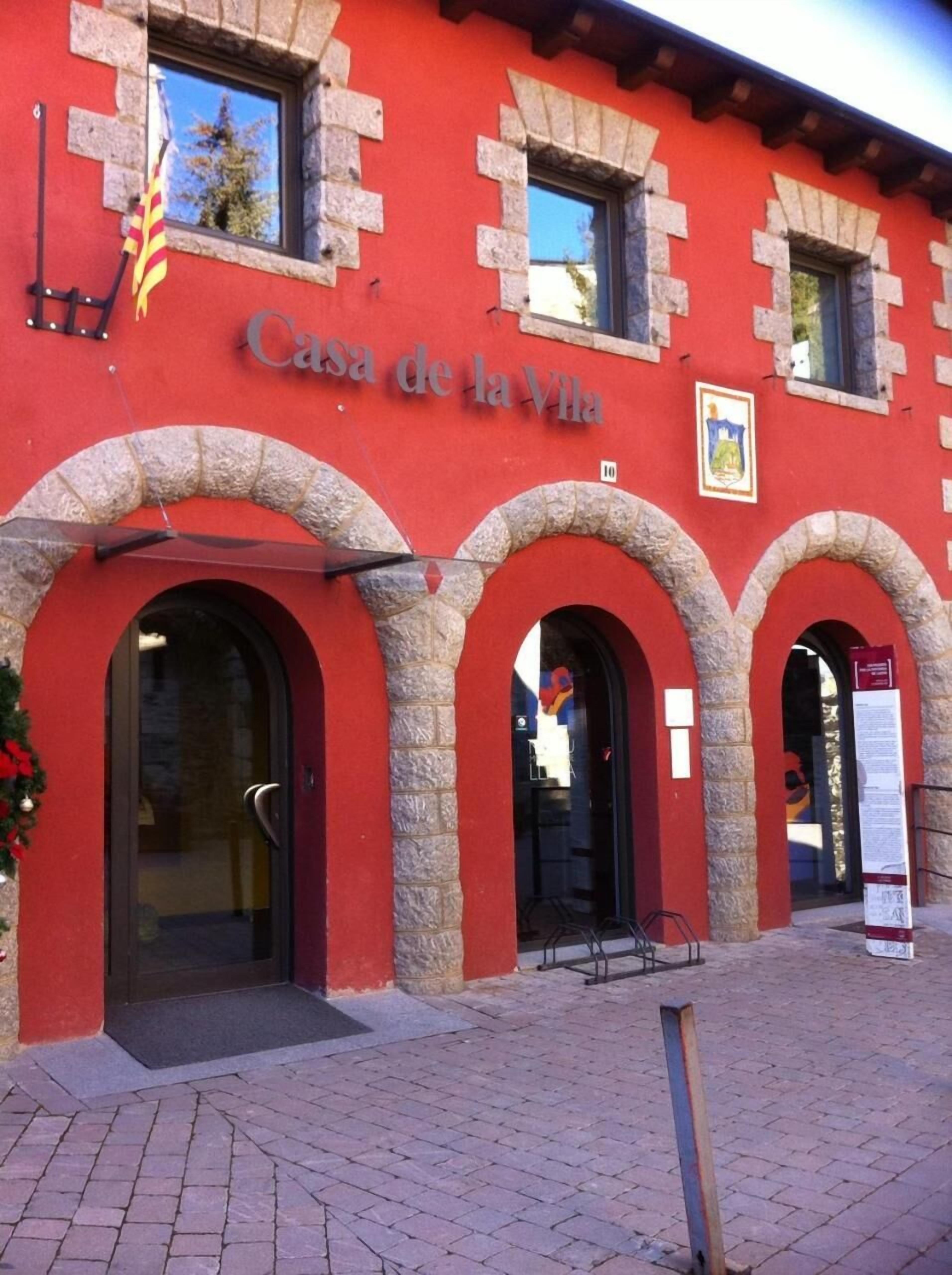 Un edificio rojo con arcos de piedra y el cartel "Casa de la Vila" sobre la entrada.