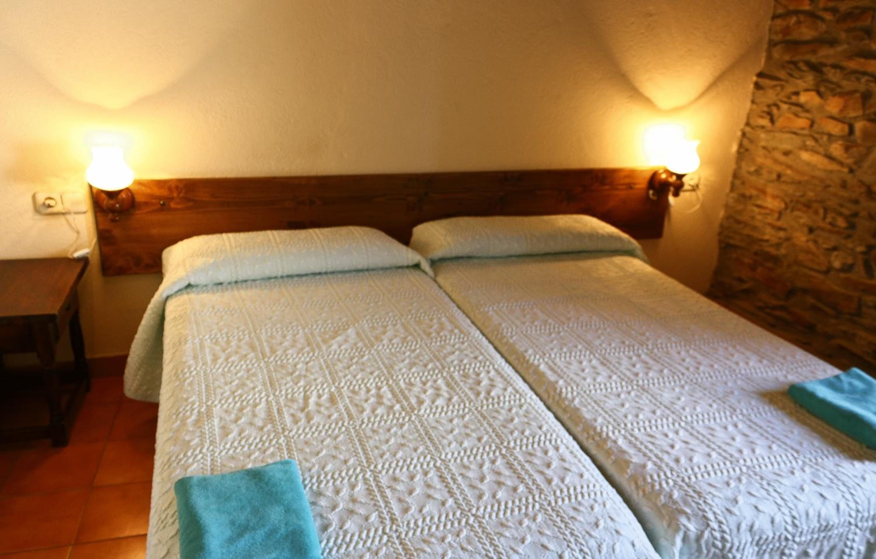 A double bed with a wooden headboard, two bedside lamps, and a stone wall.