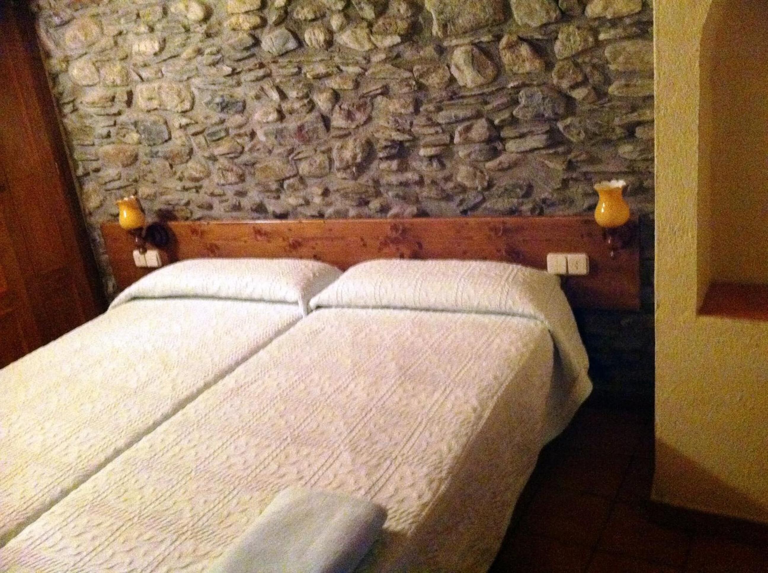A double bed with a stone wall behind it and two bedside lamps.