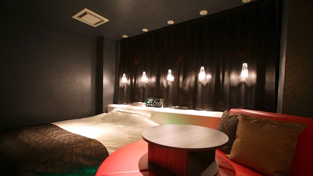 Une chambre moderne avec un lit, un canapé rouge, une table ronde et un téléviseur fixé au mur.