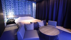 Une chambre d’hôtel moderne avec un grand lit, un coin salon doté d’une table ronde et un mur orné d’un motif.