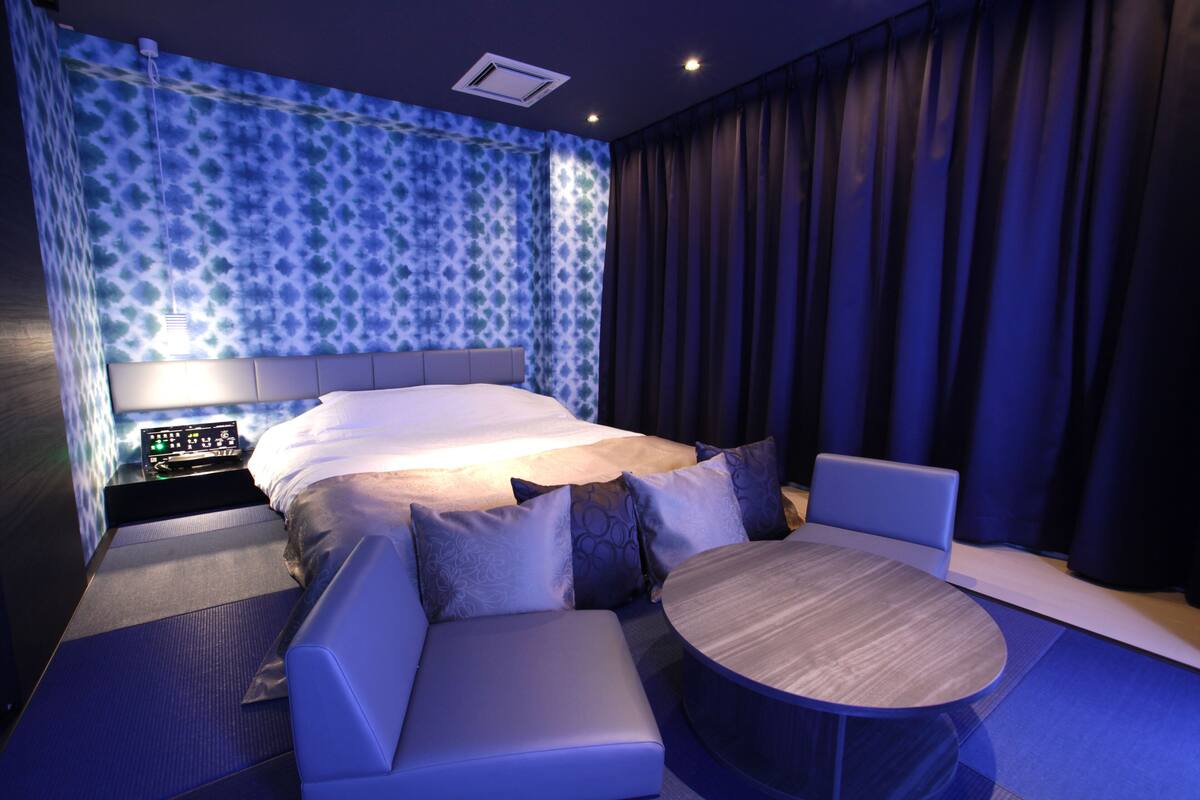 Een moderne hotelkamer met een groot bed, een zithoek met een ronde tafel en een kamerwand met een patroon.