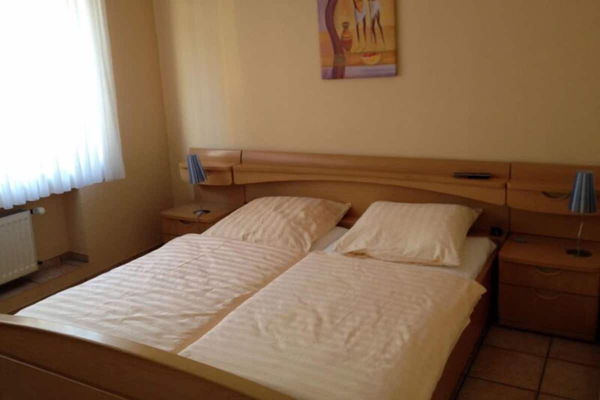 Una cama doble con dos almohadas, una mesita de noche con una lámpara y un cuadro en la pared.
