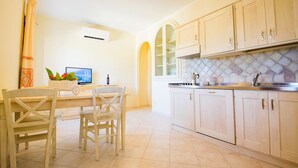 A kitchen with wooden cabinets, a dining table with chairs, and a TV. - Le Residenze del Maria Rosaria - Vico Friuli 1 (Orosei)