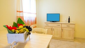 A room with a wooden table, a television on a cabinet, and a fruit basket. - Le Residenze del Maria Rosaria - Vico Friuli 1 (Orosei)