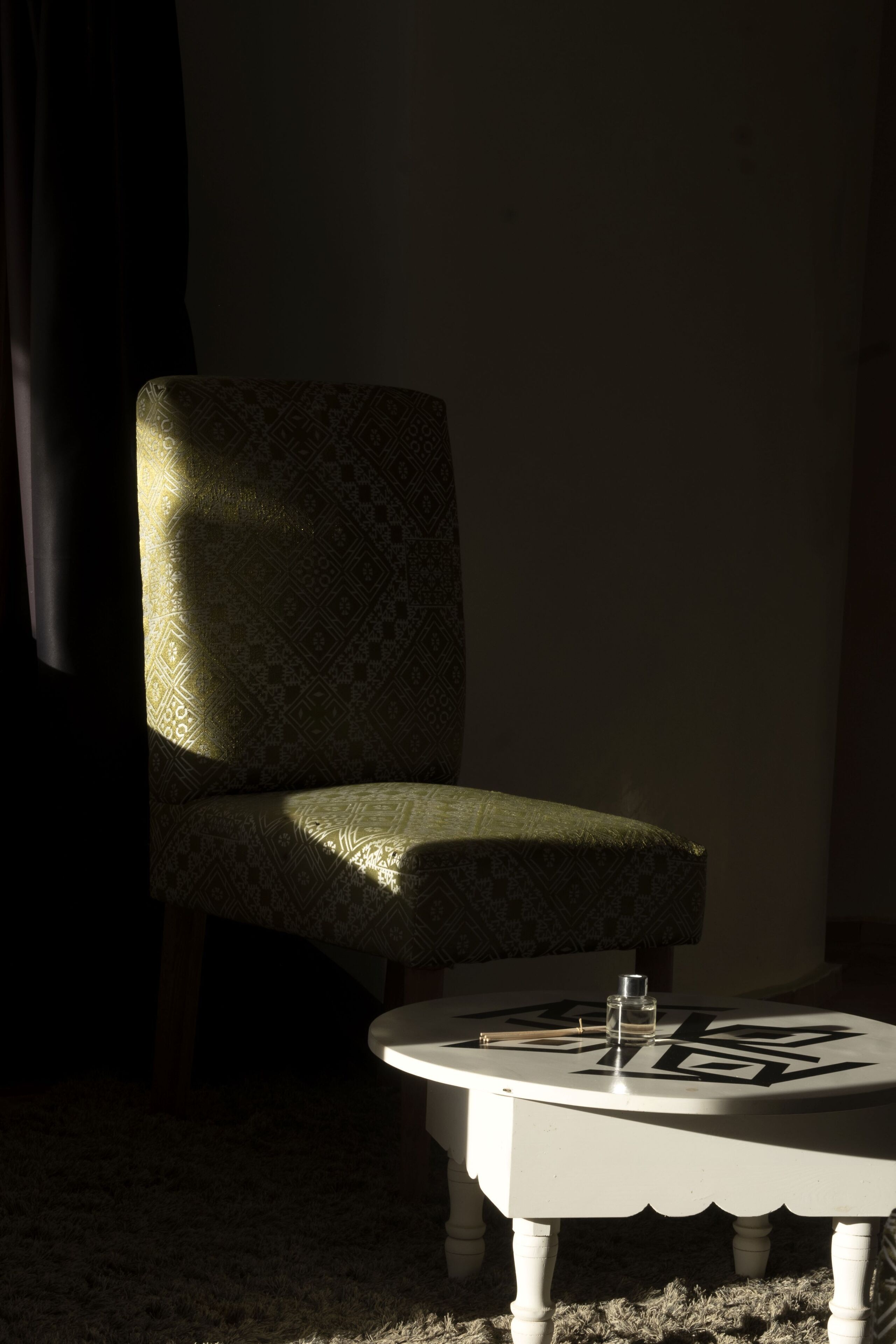 Een kamer met een gestreept fauteuil en een witte salontafel met een fles en een boek.