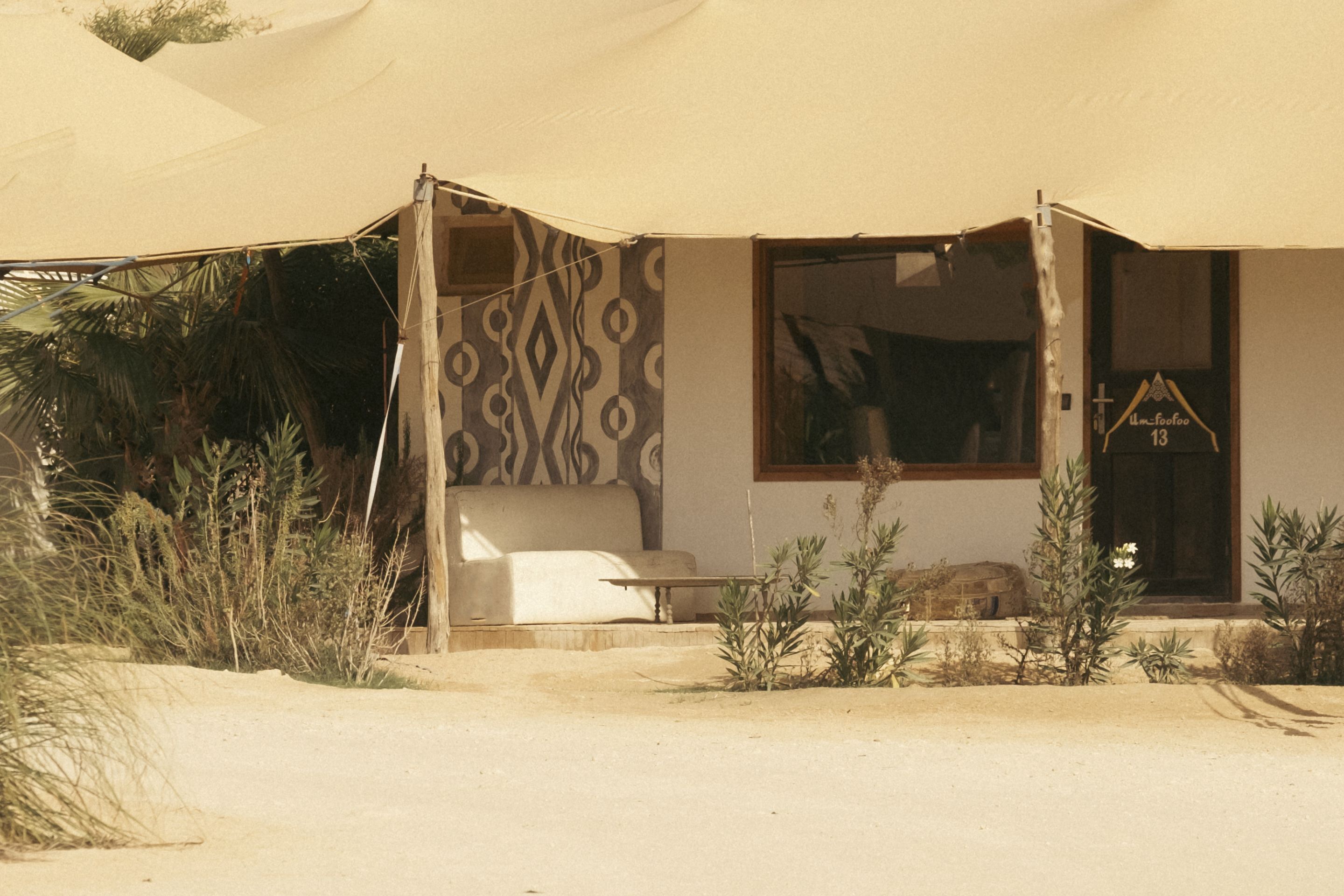 A desert-style building with a large canopy, a patterned wall, and a small garden area.