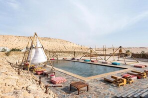 A pool area with lounge chairs and a tent structure.
