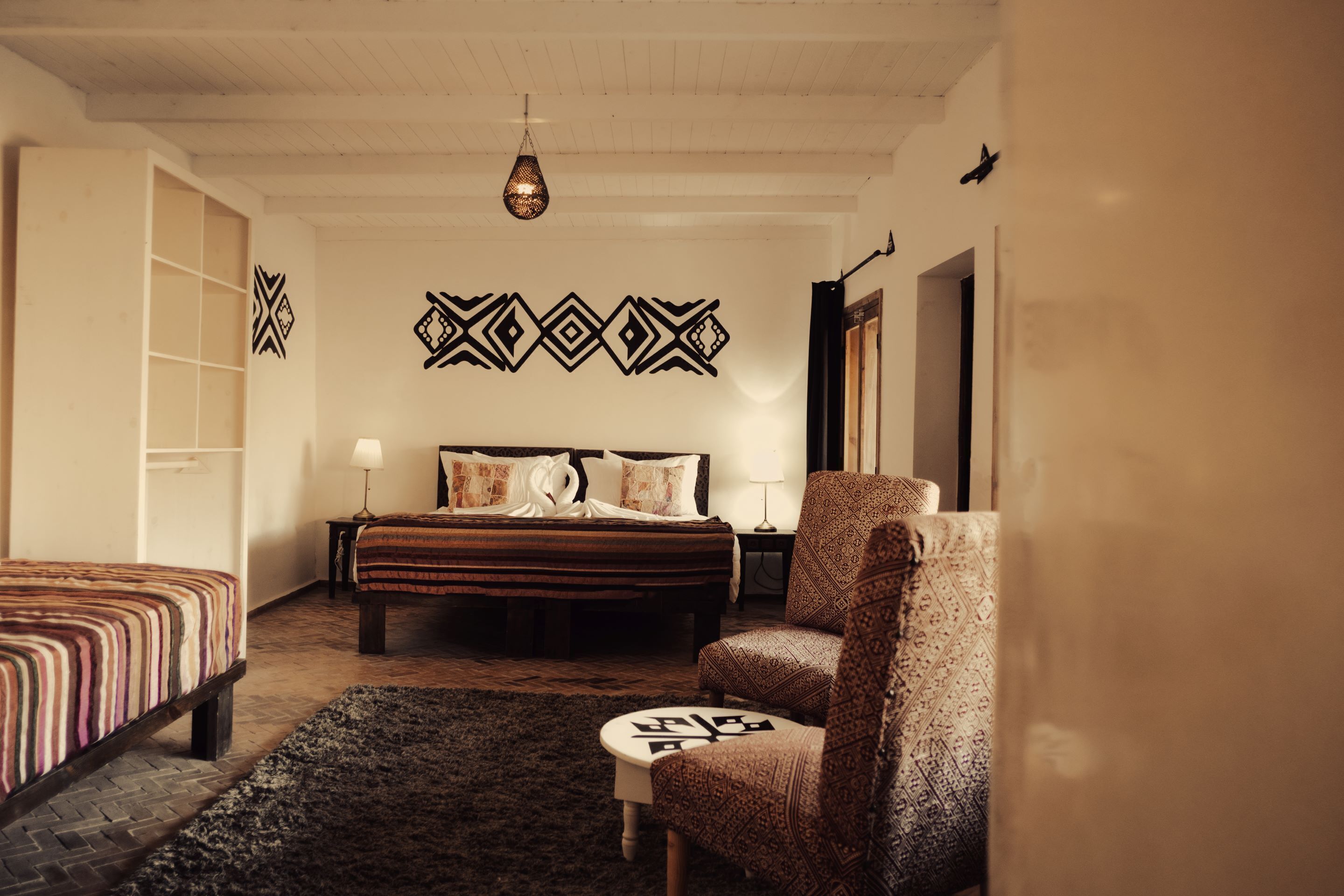 Un dormitorio con una cama grande, una silla, un tapete estampado y una pared con diseños geométricos.