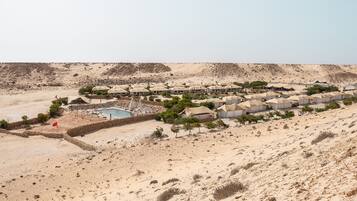 A desert resort with multiple tents, a swimming pool, and sparse vegetation.